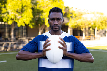 African American young male athlete holding a rugby ball on field outdoors, looking focused