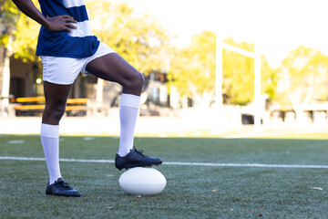 African American young male athlete standing on a rugby ball on field outdoors, copy space