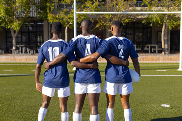 Three African American young male athletes hug on a rugby field outdoors
