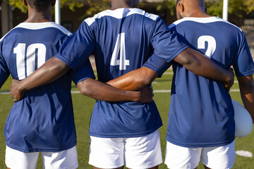 Three African American young male athletes standing together on field outdoors
