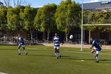 Three African American young male athletes training with a rugby ball on a field outdoors