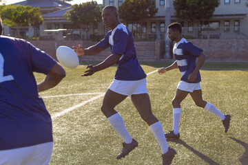 Three African American young male athletes are playing rugby on field outdoors