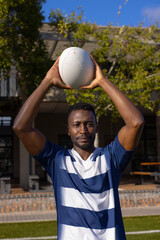 African American young male athlete holding rugby ball above head on field outdoors