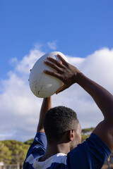 African American young male athlete holding a rugby ball, ready to throw, copy space