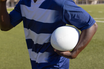 African American young male athlete in striped sports shirt holding rugby ball on field outdoors