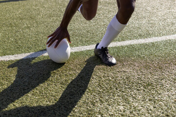 An African American young male athlete wearing sports gear is placing a rugby ball on the grass