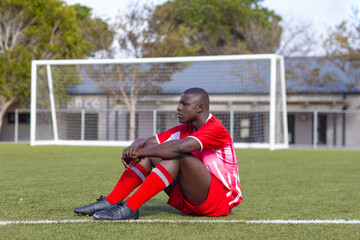 African American young male athlete sitting on soccer field outdoors, looking thoughtful, copy space