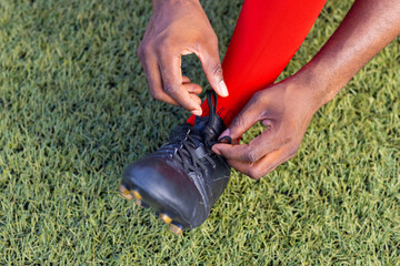 African American young male athlete tying shoelaces on a soccer field outdoors, copy space