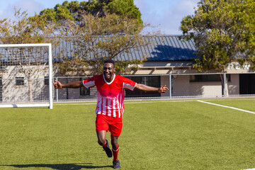 African American young male athlete wearing red and white soccer uniform running on field outdoors