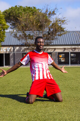 Obraz premium An African American young male athlete in red sportswear is celebrating on field outdoors