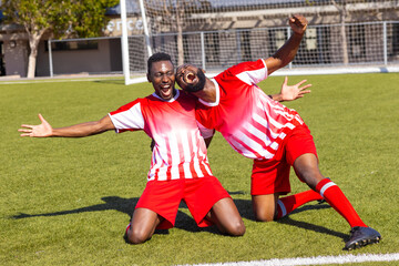 Two African American young male athletes are celebrating on a soccer field outdoors