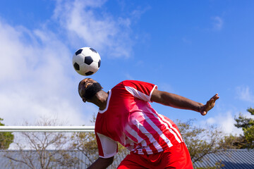 African American young male athlete in striped red & white shirt heads soccer ball on field outdoors