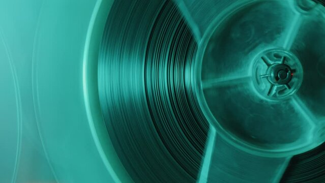 Part of rotating reel tape of vintage analog tape recorder playing the music in the studio with blue neon light. Macro shot