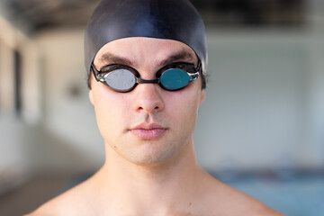 Caucasian young male swimmer wearing goggles and cap is ready to swim indoors