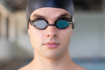 Caucasian young male swimmer wearing goggles and cap, looking focused indoors