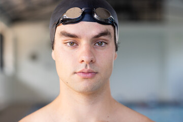 Caucasian young male swimmer wearing goggles preparing for training indoors