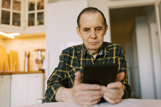 Senior man using modern digital tablet at home for video call
