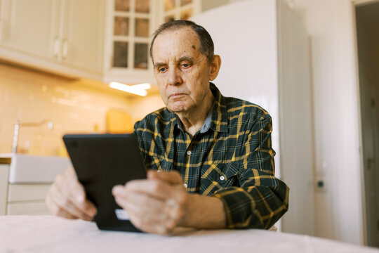 Senior man using modern digital tablet at home for video call