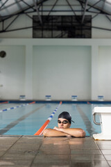 Caucasian young male swimmer resting at pool edge indoors, looking away, copy space