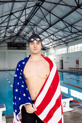 Caucasian young male swimmer, indoors, wrapping in American flag stands by pool