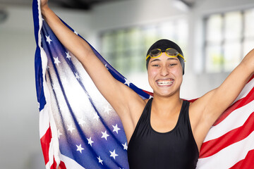 Biracial young female swimmer holding American flag indoors, wearing goggles, smiling