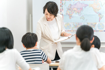 塾・学校の教室で小学生・中学生の子供に勉強を教える女性講師・教師
