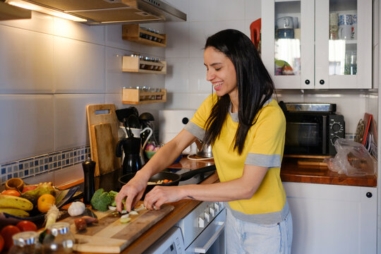 Smiling Woman in the kitchen preparing vegetables on pan on stove