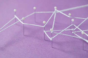 White thread tying straight pins on violet papercraft background