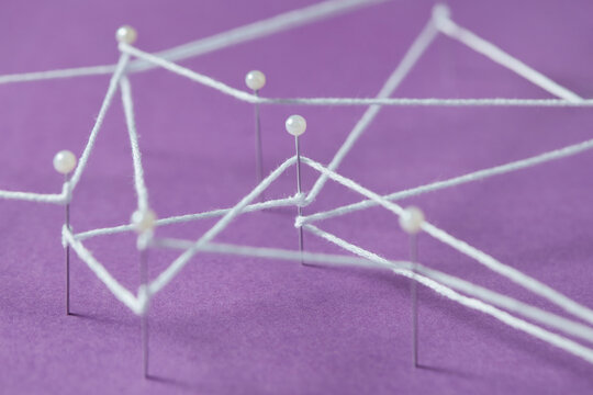Straight pins connecting with white thread on violet background