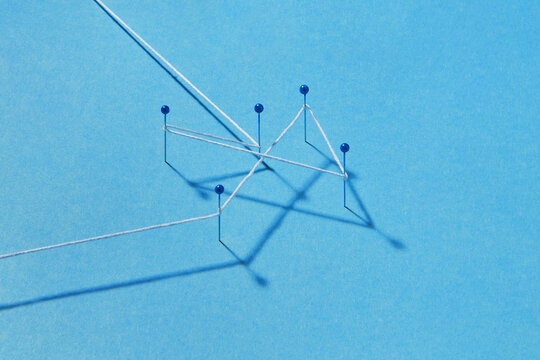 White thread connecting push pins on blue paper background