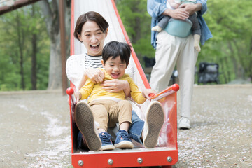 Fototapeta na wymiar 新緑の公園の滑り台で遊ぶアジア人（日本人）の親子 4人家族　子育てや育児の休日のイメージ