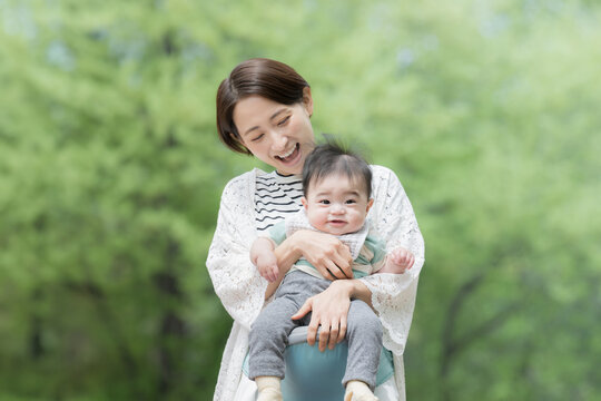 A mother (mother) holding her baby in a fresh green park Image of bright childcare, child rearing, and lifestyle
