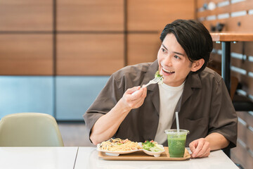 カフェでランチ・パスタを食べる若いアジア人男性
