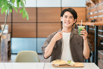 カフェでランチを食べながらグリーンスムージーを飲む若い男性（酵素・デトックス・食物繊維・健康食品）
