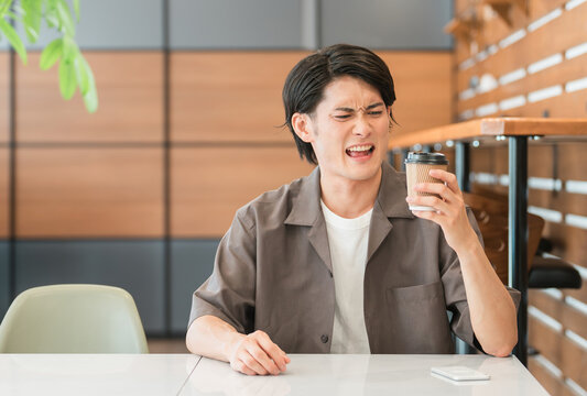 不味そうにコーヒーを見つめるアジア人男性（まずい・がっかり・失敗・睨む）
