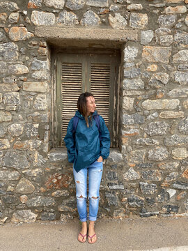 A young girl in torn jeans stands leaning against the wall.