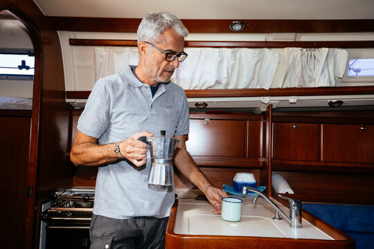 Elderly man making coffee in galley kitchen of sailboat