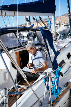 Senior helmsman checking documents while sitting on sailboat
