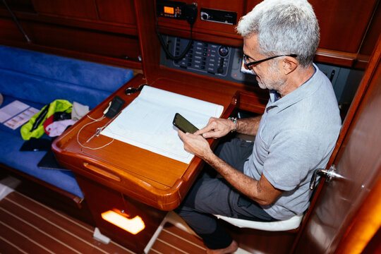 Middle age man browsing smartphone while sitting at table in yacht