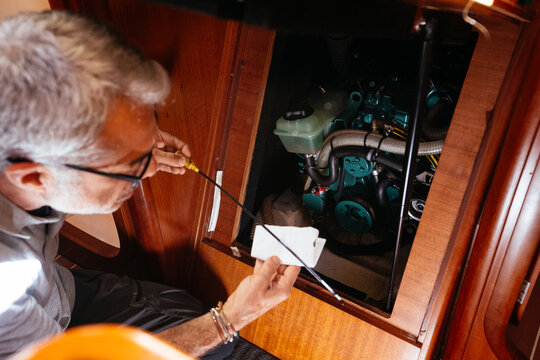 Senior mechanic checking oil level of engine on yacht with dipstick