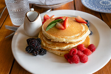 stack of pancakes with strawberries, blackberries, and raspberries on a white plate with a small...