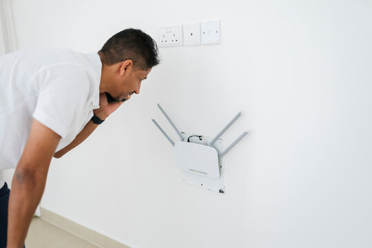 Smiling man having phone conversation while inspecting Wi Fi router