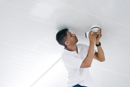Focused male worker mounting surveillance camera on ceiling