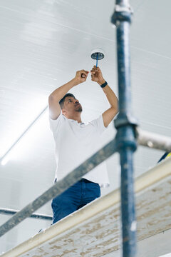 Young man installing security camera on ceiling of modern building