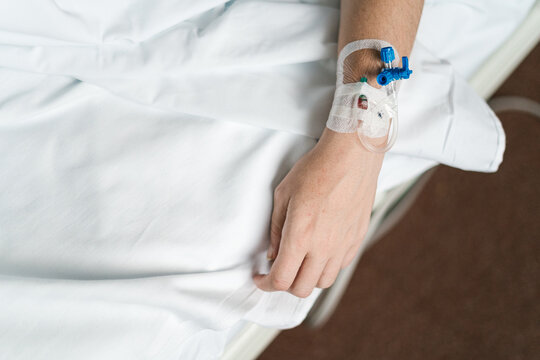 Crop hand of patient receiving saline solution with IV drip