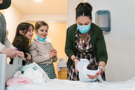 Girls watching mother wrapping baby on bed in hospital