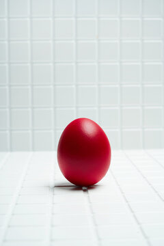 Red Egg Standing on White Table Against Tiled Background