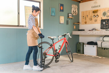 自宅の車庫でロードバイクのタイヤに空気を入れる若いアジア人女性
 - obrazy, fototapety, plakaty