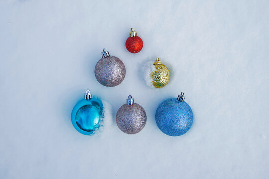 Christmas tree toys balls of blue, yellow and red colours are laid out on snow in shape of Christmas tree