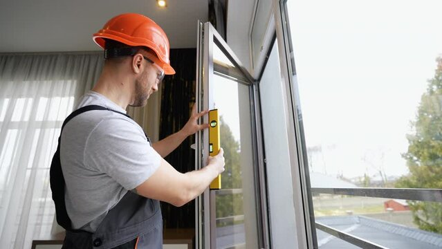 Window installer adjusting plastic windows with level tool in room at home
